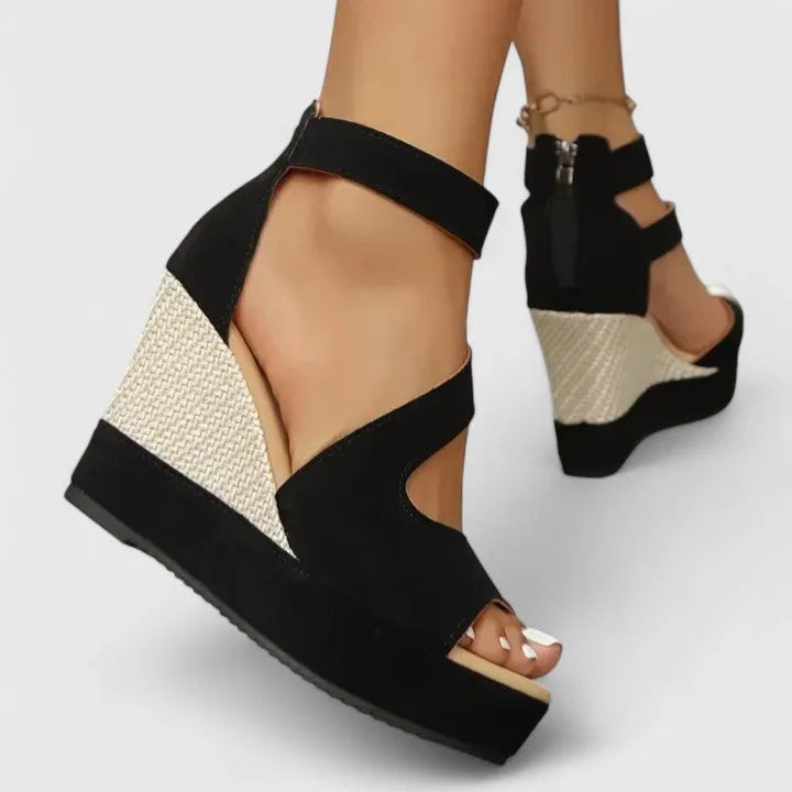 Back view of ankles in black wedge sandals highlighting the zip closure and woven wedge heel