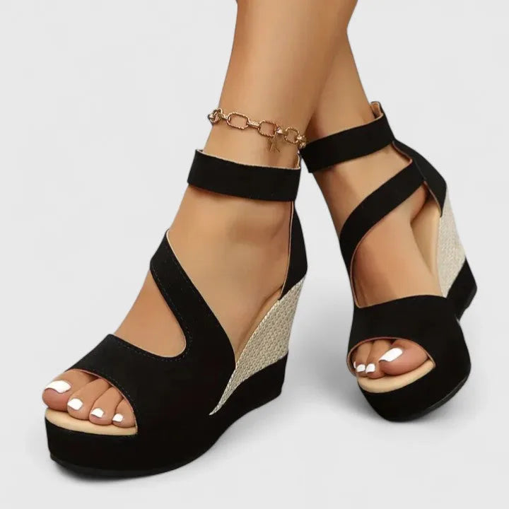 Side view of black suede wedge sandals showing the curved ankle strap and textured platform sole
