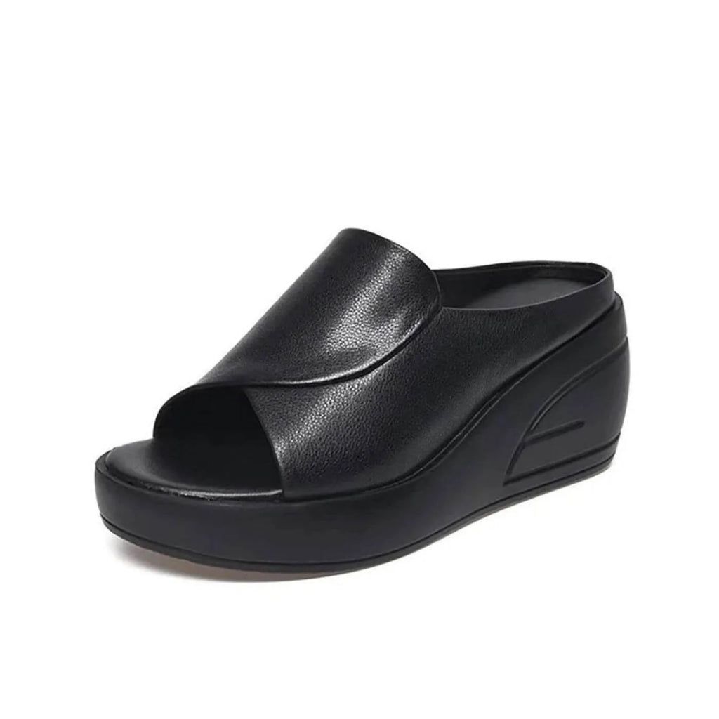 Angled view of a black leather wedge slide with crossover peep toe and ribbed platform sole