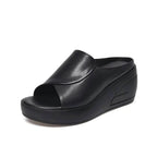 Angled view of a black leather wedge slide with crossover peep toe and ribbed platform sole