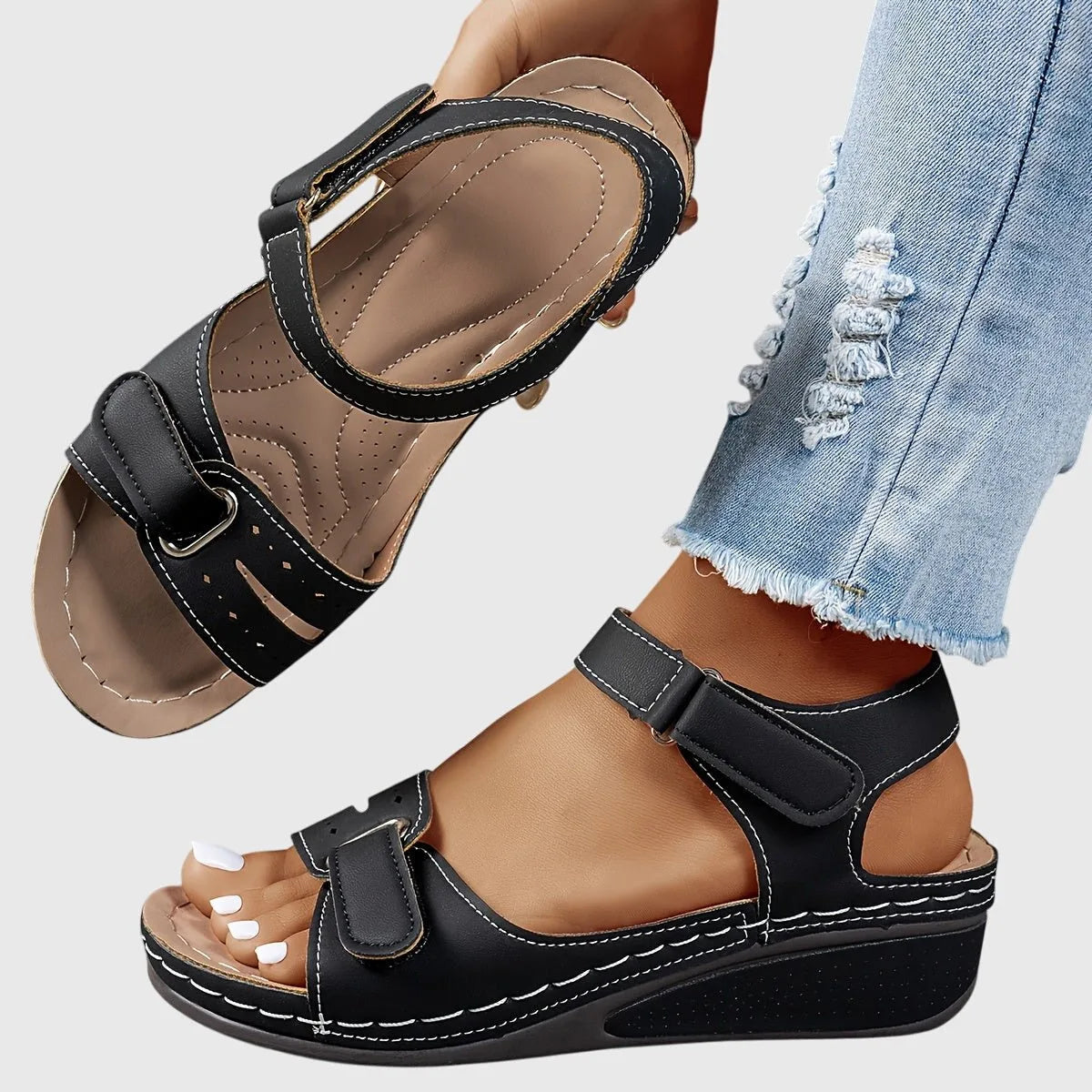 Black wedge sandal pair, top sandal tilted to show the cushioned insole and perforated strap detailing