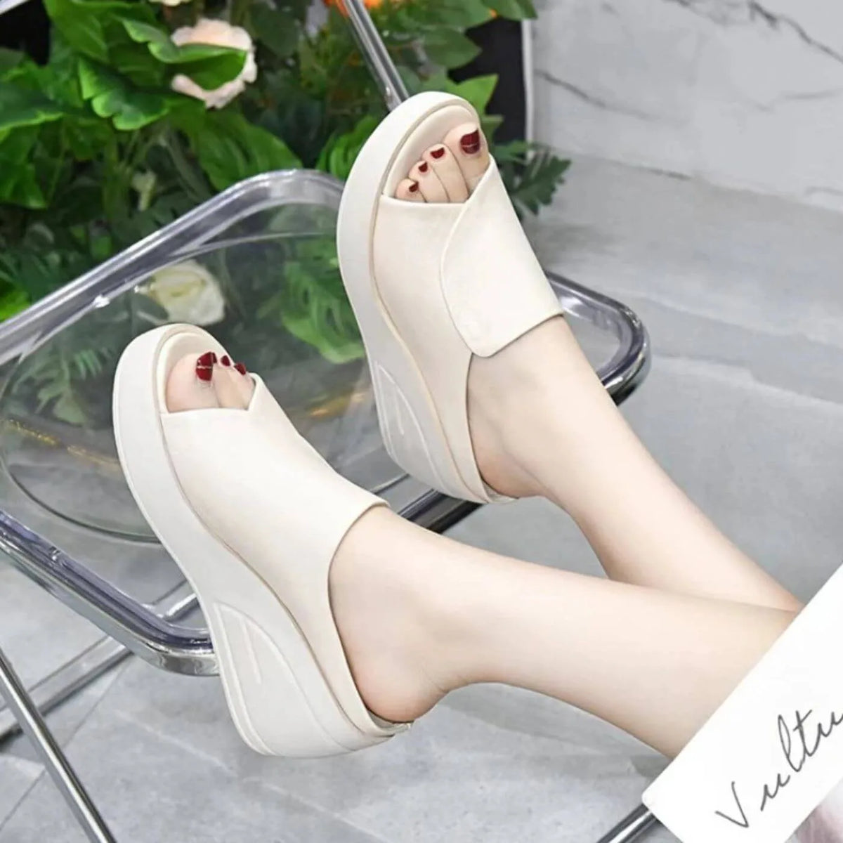 Model wearing beige wedge slides on a clear chair, side view highlighting the crossover toe strap