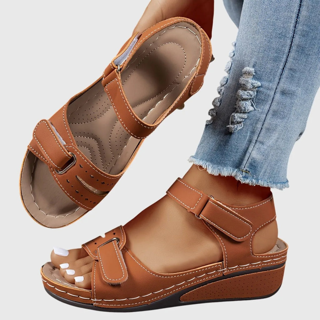 Brown wedge sandal worn on foot with matching sole, paired with ripped denim jeans