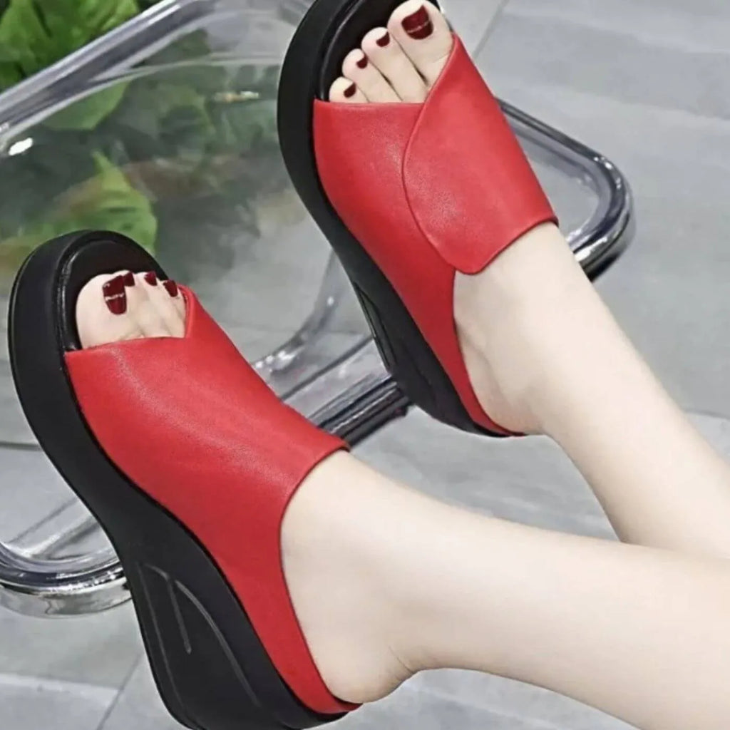 Close-up of red wedge slides worn on feet, showing soft leather upper and black platform wedge sole