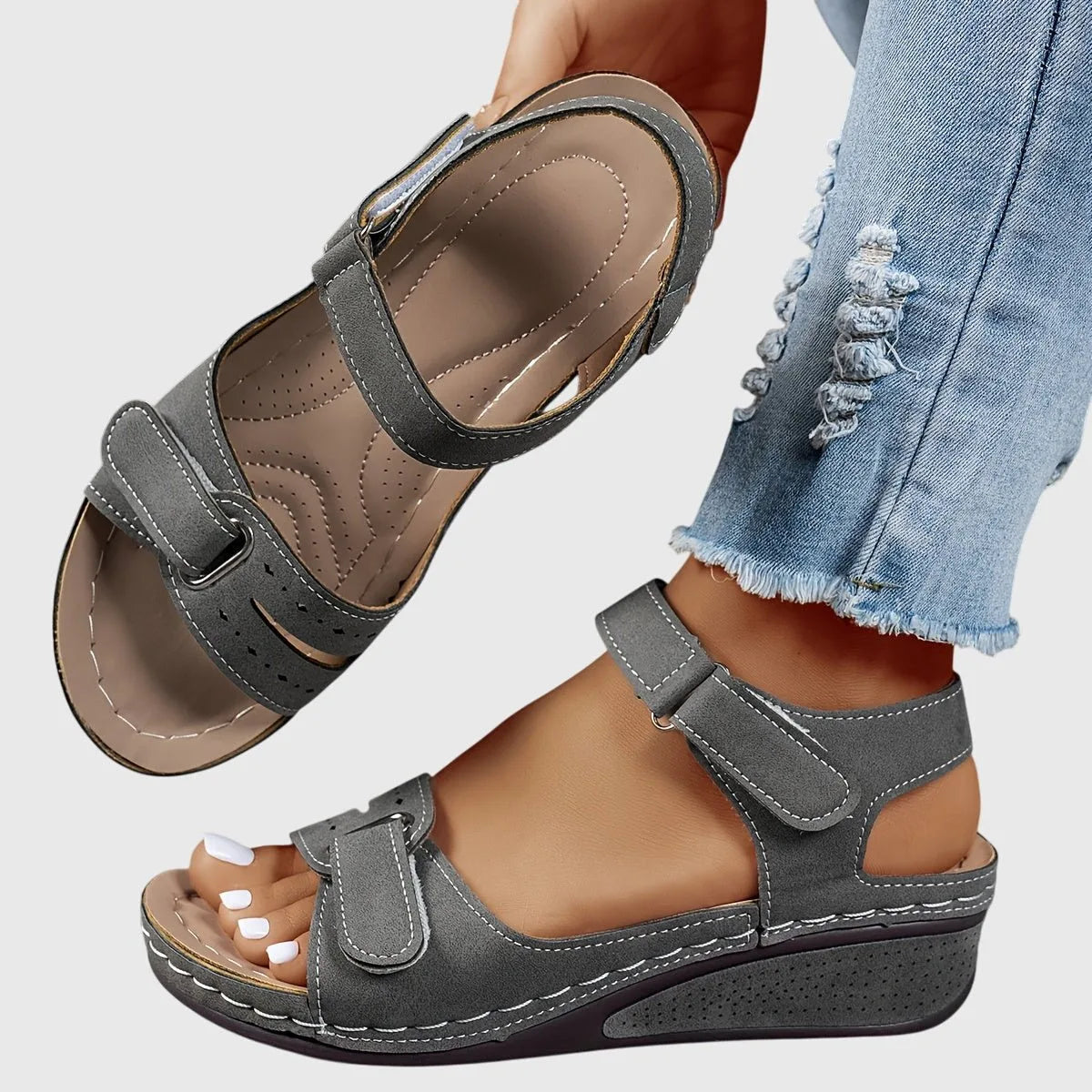 Mid grey suede-look wedge sandal with contrast stitching, one shoe held above the worn pair