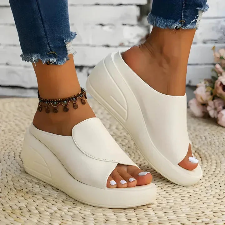 Beige wedge slide shown from the side on foot, paired with denim, resting on a woven jute mat