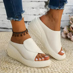 Beige wedge slide shown from the side on foot, paired with denim, resting on a woven jute mat