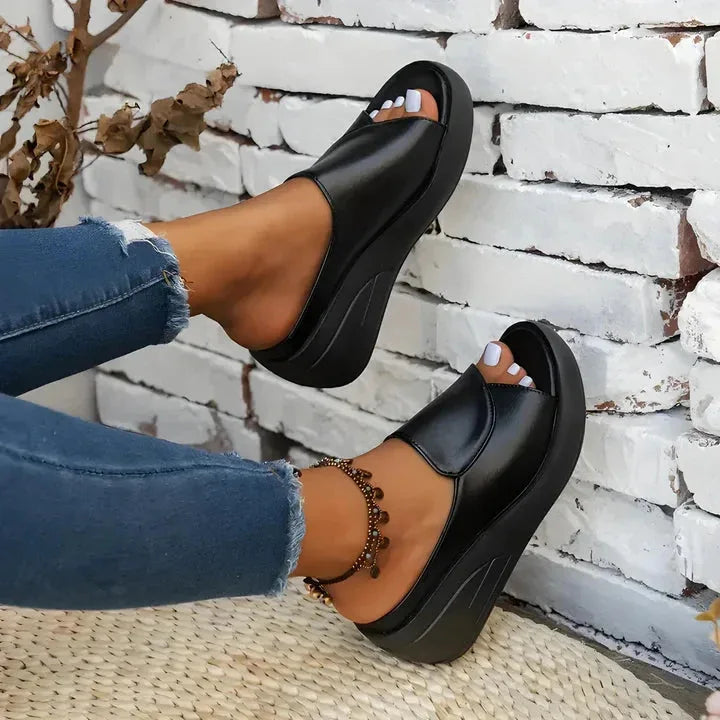 Black wedge slide worn with cropped jeans, back angle showing the chunky ridged wedge heel