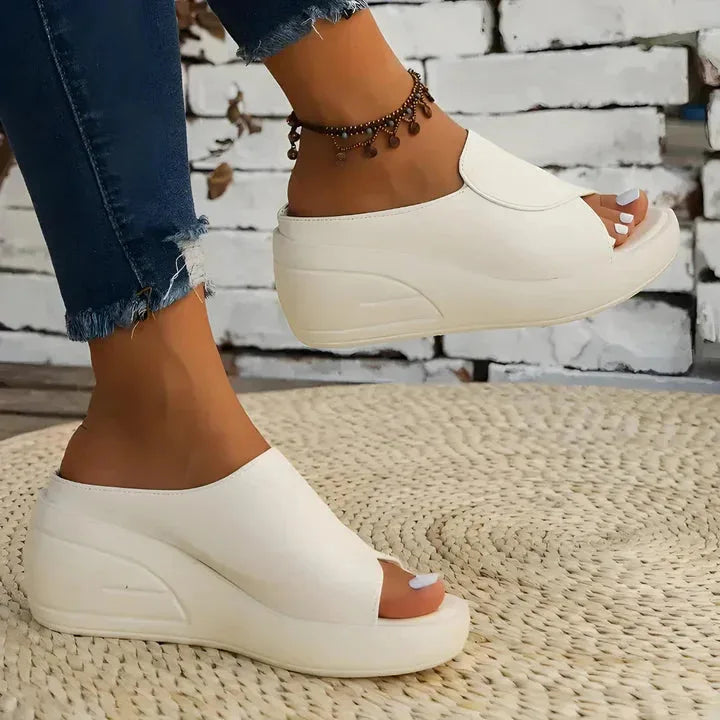 Beige wedge slide shown mid-step with foot lifted, highlighting the thick platform sole