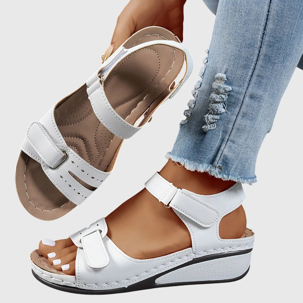 White wedge sandal pair with tan footbed, one shoe raised to show the anatomical arch contouring