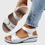 White wedge sandal pair with tan footbed, one shoe raised to show the anatomical arch contouring