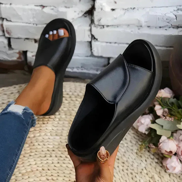 Black slip-on wedge slide held in hand, showing the plush padded toe panel and smooth sole