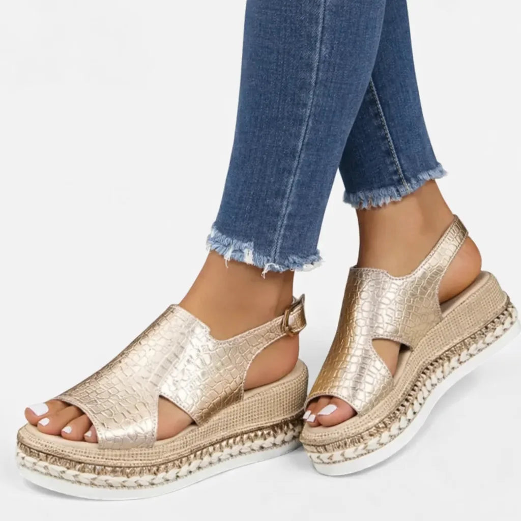 Side profile of gold croc-print wedge sandal with ankle buckle strap paired with cuffed denim jeans