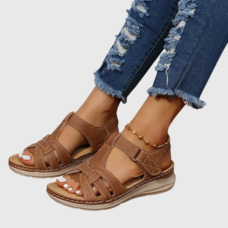 Side view of tan brown woven leather gladiator sandal with cushioned wedge sole, worn with ripped denim jeans