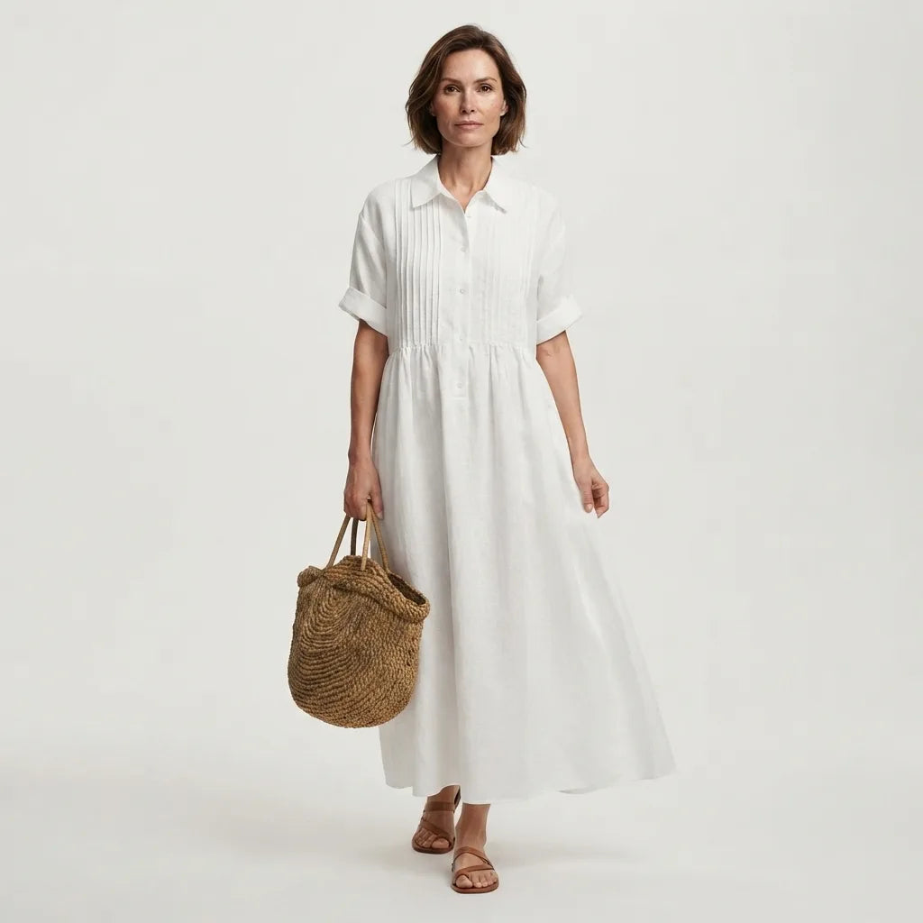 Front view of a woman wearing a white pintuck linen-look maxi shirt dress with a straw tote bag, standing against a plain backdrop