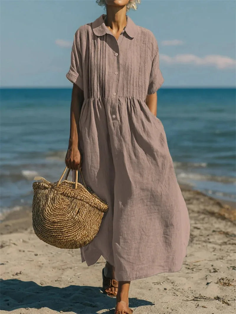 Model walking on the beach in the dress in a mustard yellow shade against a clear blue sky