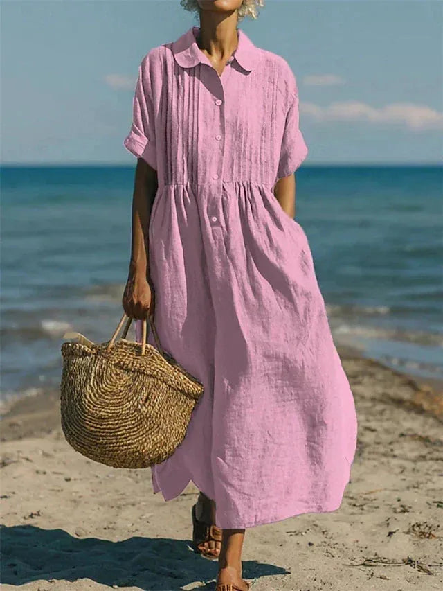 Model walking along the shore in the dress in pink, with the sea and sandals visible