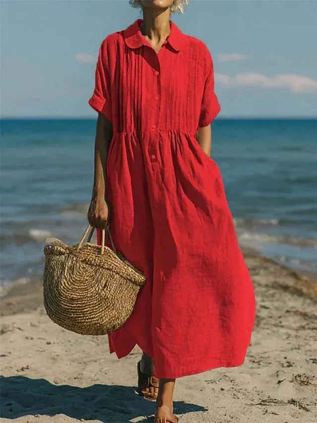 Model walking by the water in the dress in bright red, with straw tote bag in hand