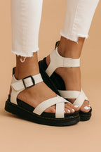 Close-up side view of white vegan leather platform sandals with crossover straps and black chunky sole