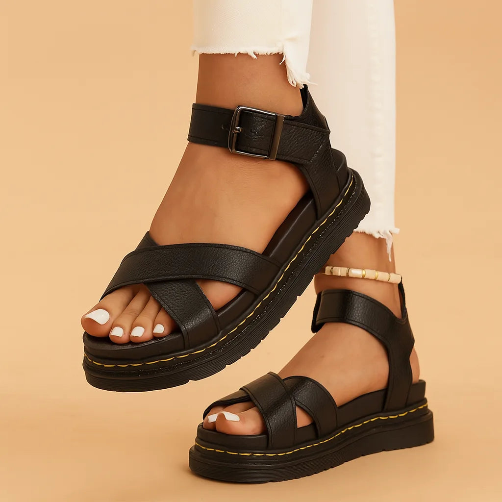 Black platform sandals with crisscross toe straps and adjustable ankle buckle on a black ridged sole
