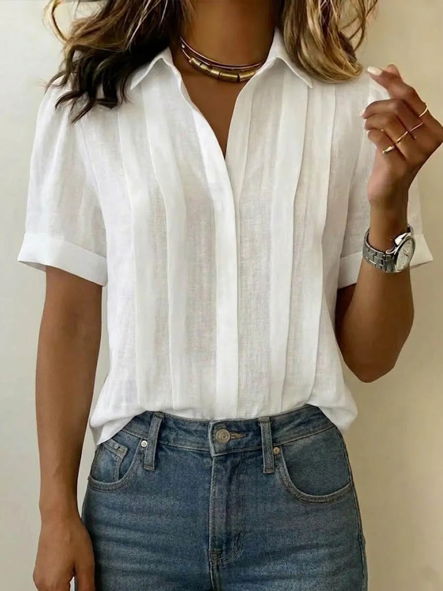 Close-up of a white pleated linen blouse with V-neck collar, worn with denim and a gold layered choker