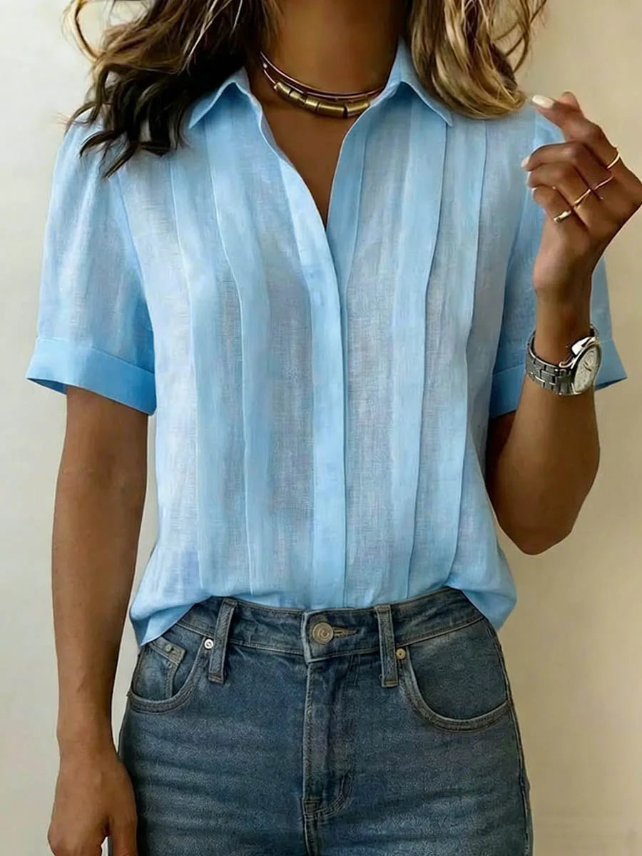 Light blue pleated linen blouse with open collar and rolled short sleeves, paired with denim jeans