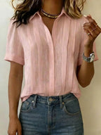 Soft pink pleated linen blouse with V-neckline and folded cuffs, styled with a gold choker necklace