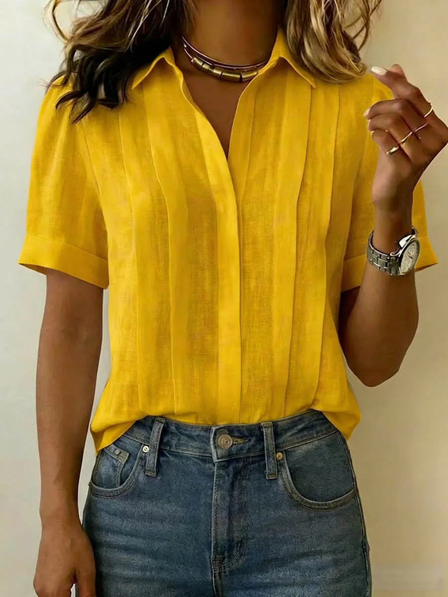 Mustard yellow pleated linen blouse with collared V-neck and short sleeves, worn over blue denim jeans