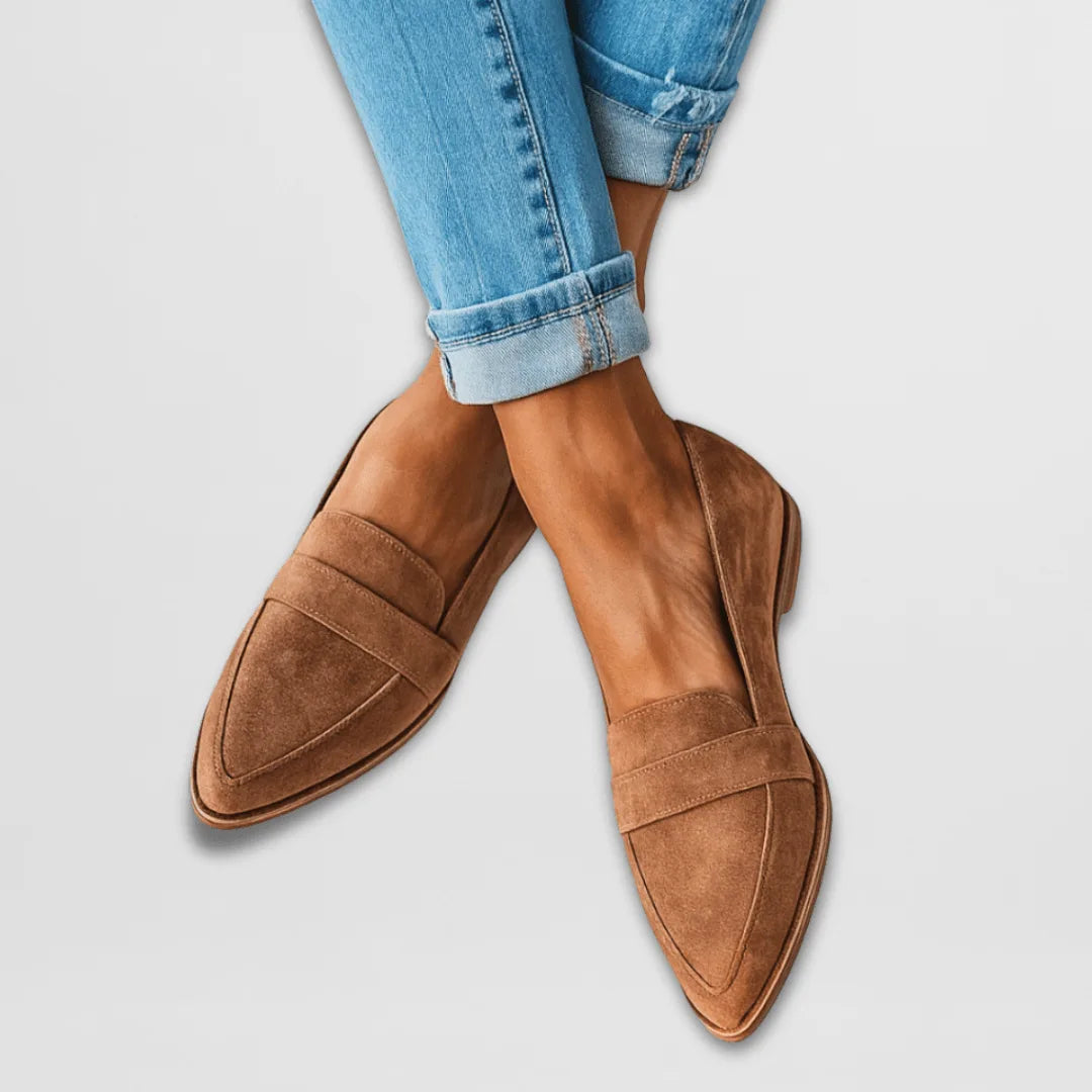 Tan suede pointed-toe loafers with penny strap detail worn with cuffed blue jeans, crossed-leg pose
