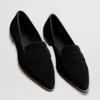 Black suede pointed-toe loafers with penny strap detail, side angle on a plain background