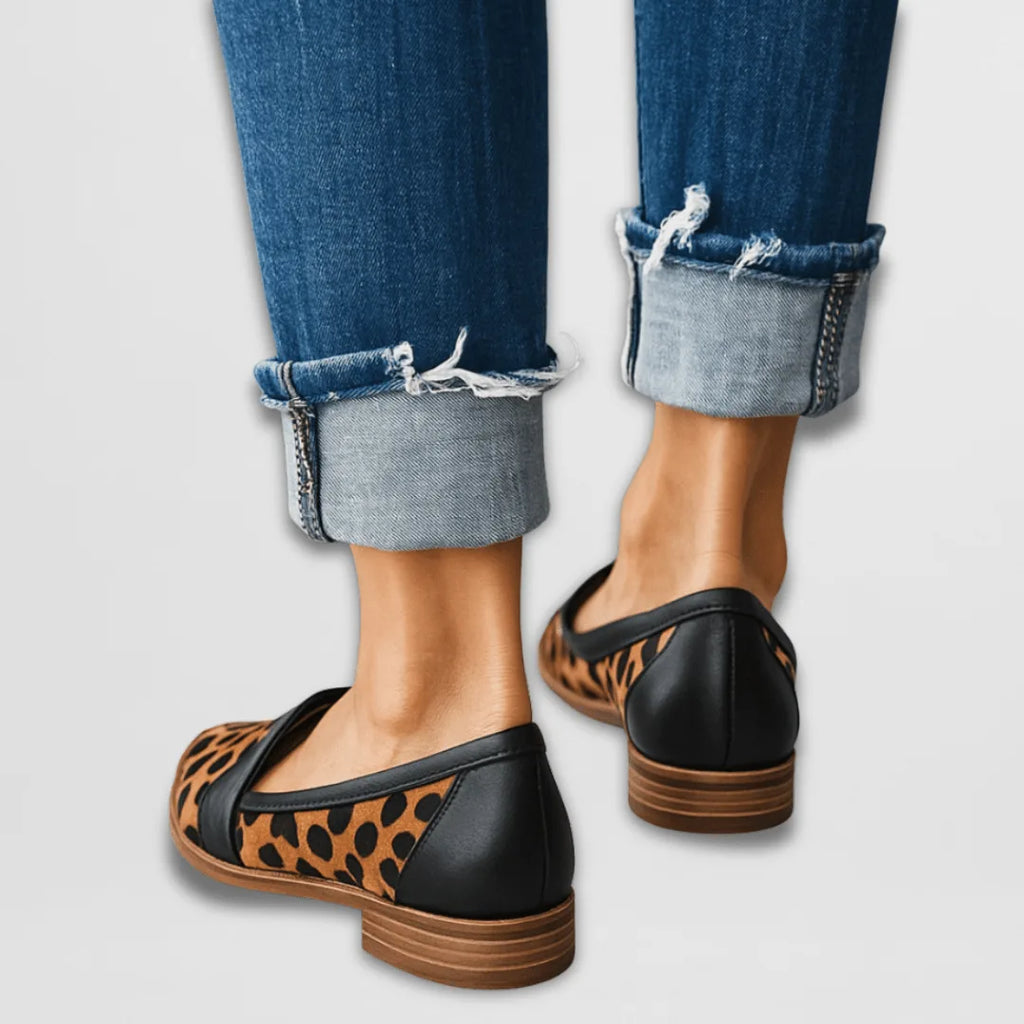 Rear view of leopard-print loafers with black heel trim and stacked wooden-look heel, denim cuffs above