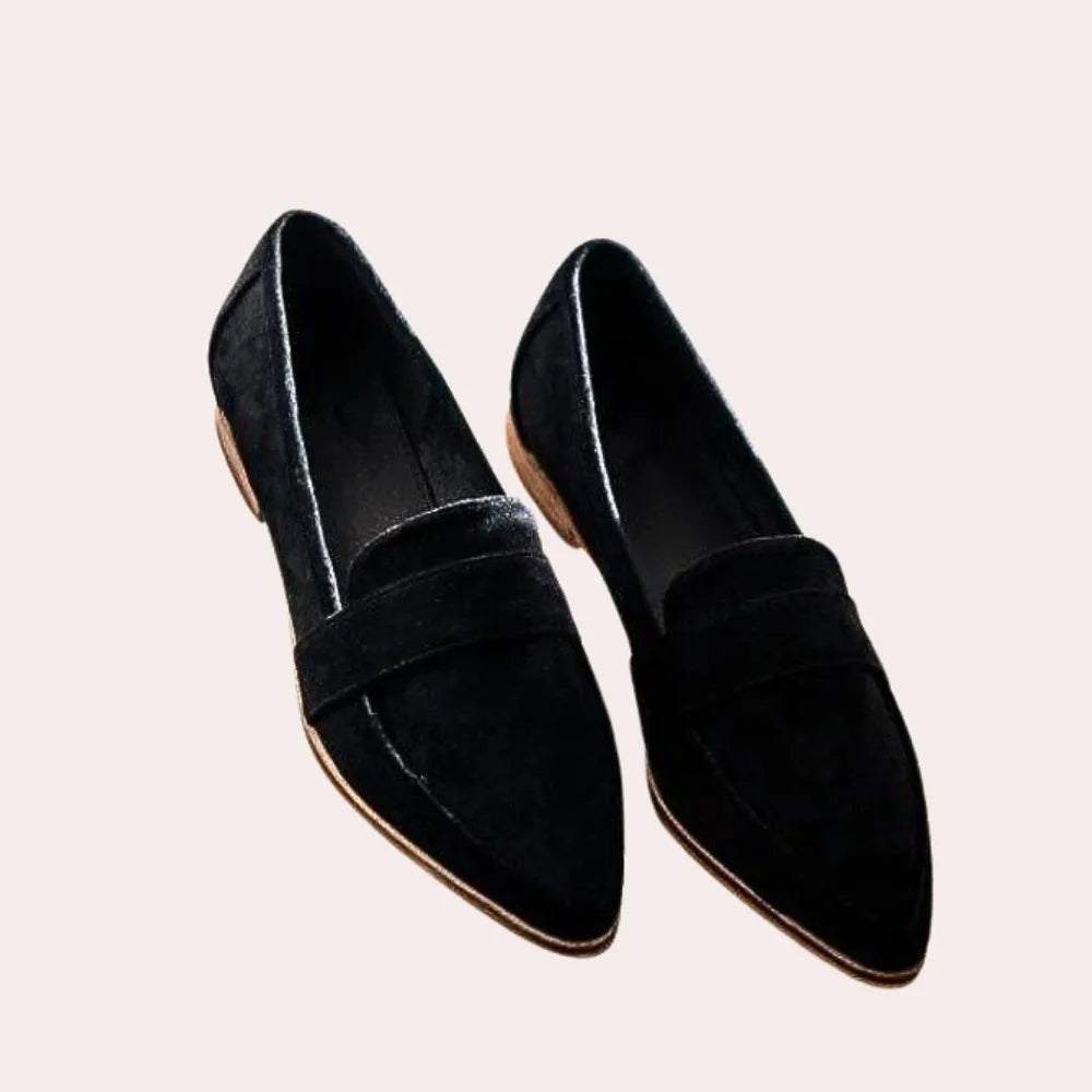 Top-down view of black suede pointed-toe penny loafers with stacked block heel on a pink backdrop
