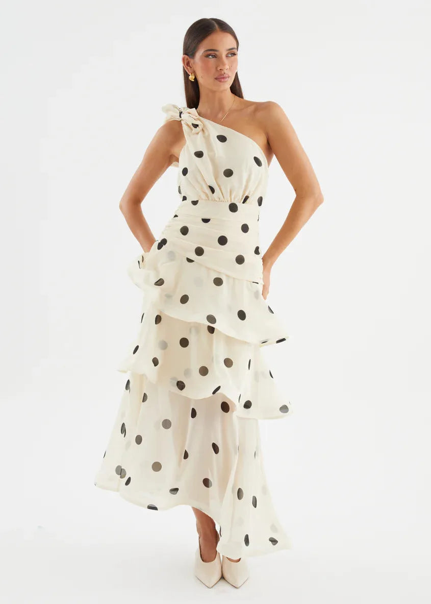Three-quarter view of the cream polka dot dress showing the asymmetric one-shoulder neckline and bow