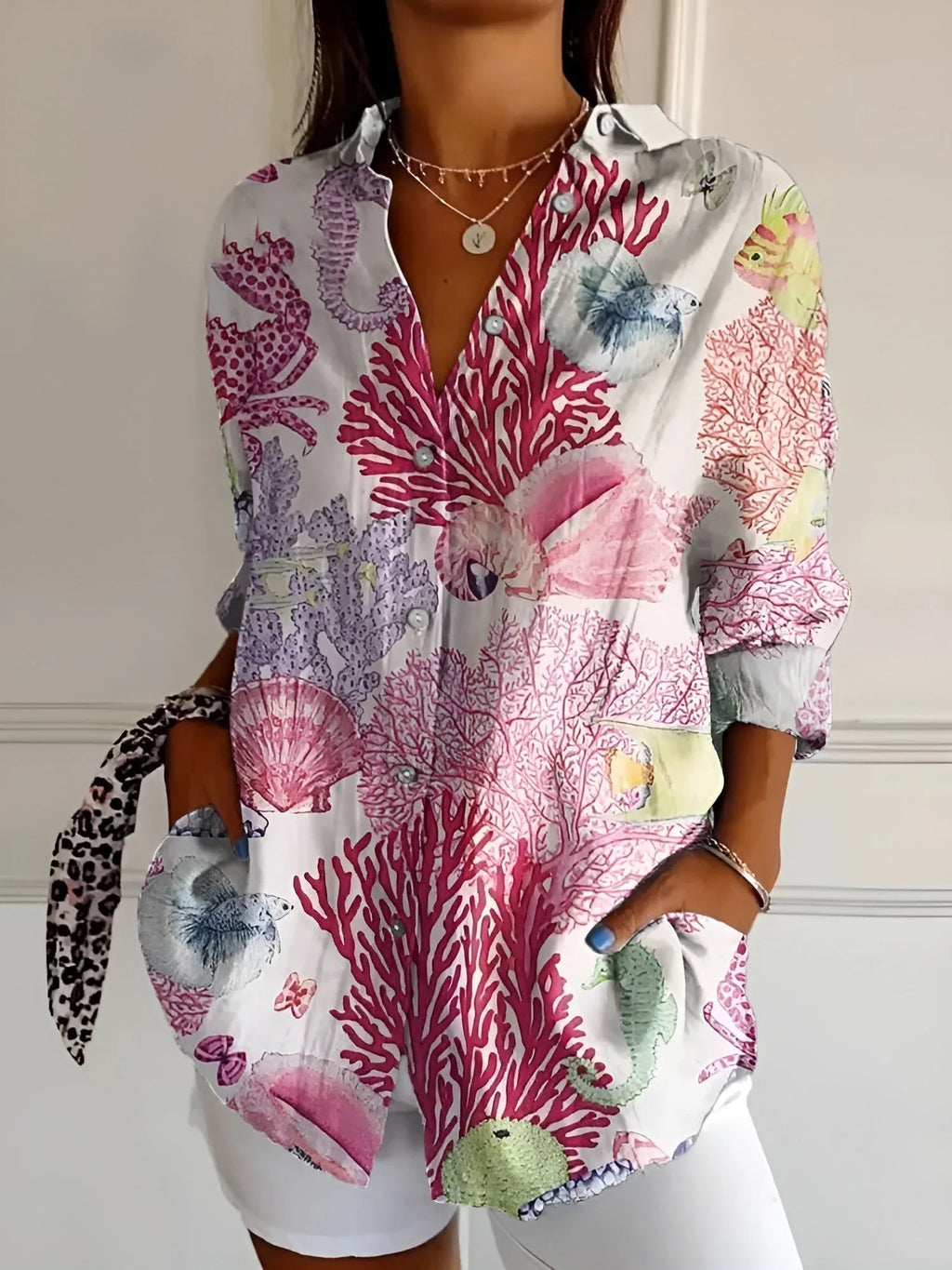 Close-up of a white printed blouse with pink coral, seahorse and fish motifs, worn open over a white outfit