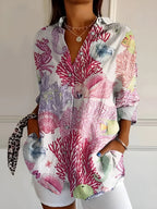 Close-up of a white printed blouse with pink coral, seahorse and fish motifs, worn open over a white outfit
