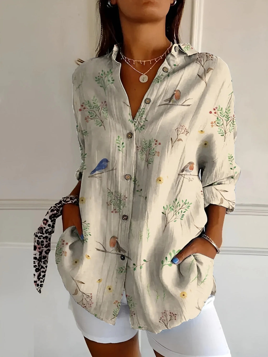 Beige button-up blouse printed with small birds and botanical sprigs, shown with front patch pockets