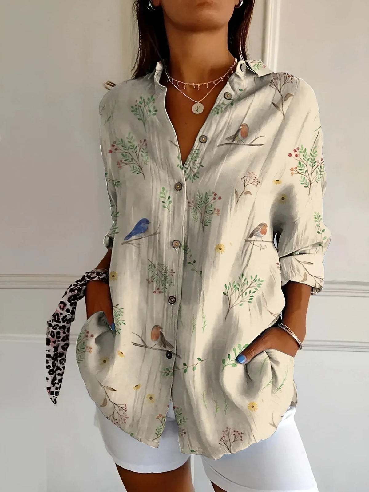 Beige button-up blouse printed with small birds and botanical sprigs, shown with front patch pockets