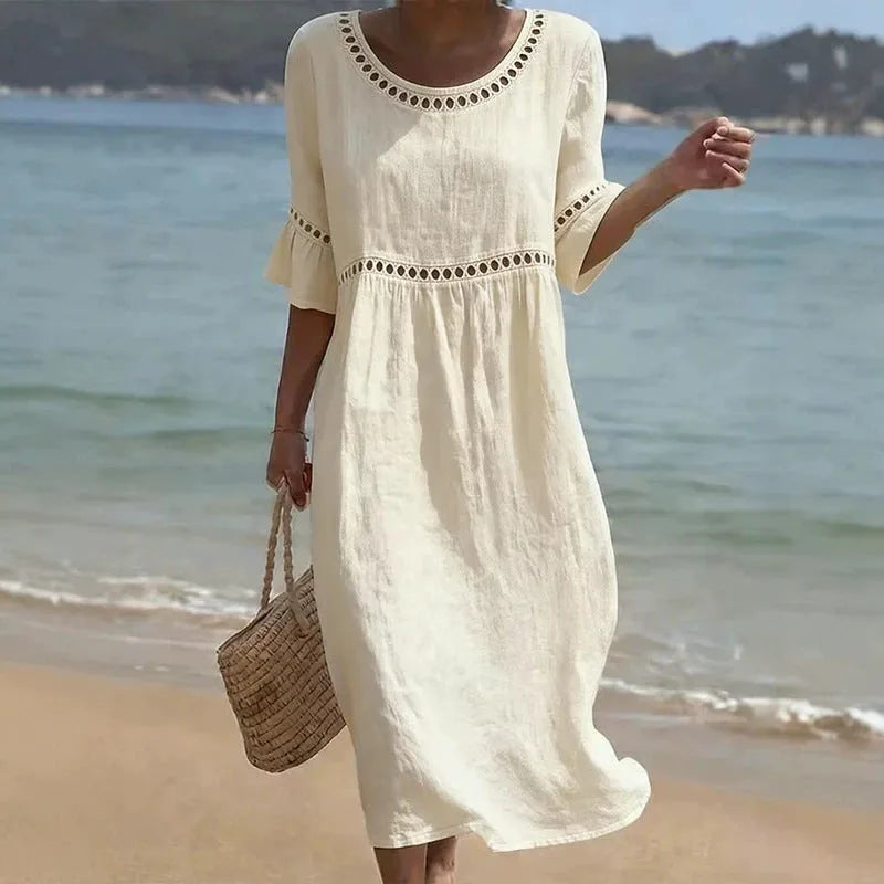 Woman on a beach wearing a cream linen-look midi dress with hollow out neckline trim and flared sleeves