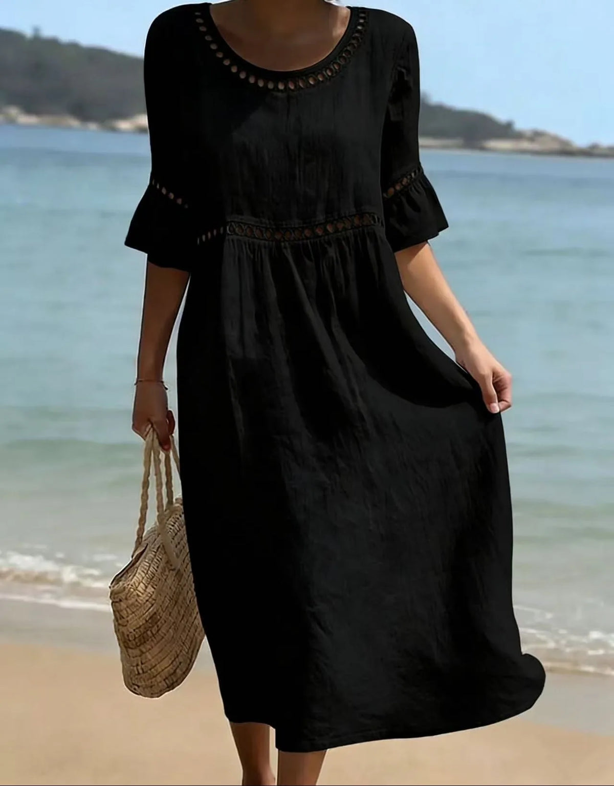 Model standing on the beach in a black midi dress with hollow out waist trim and flared cuff sleeves