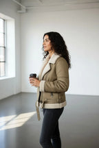 Side profile of the khaki aviator jacket showing the shearling cuff and collar detail while holding a coffee cup