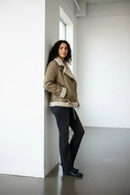 Full-length side view of the aviator jacket with belt tied at the waist, paired with dark denim and ankle boots