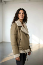 Close-up side view of the aviator jacket highlighting the front zip, buckled tab and shearling trim on the sleeve