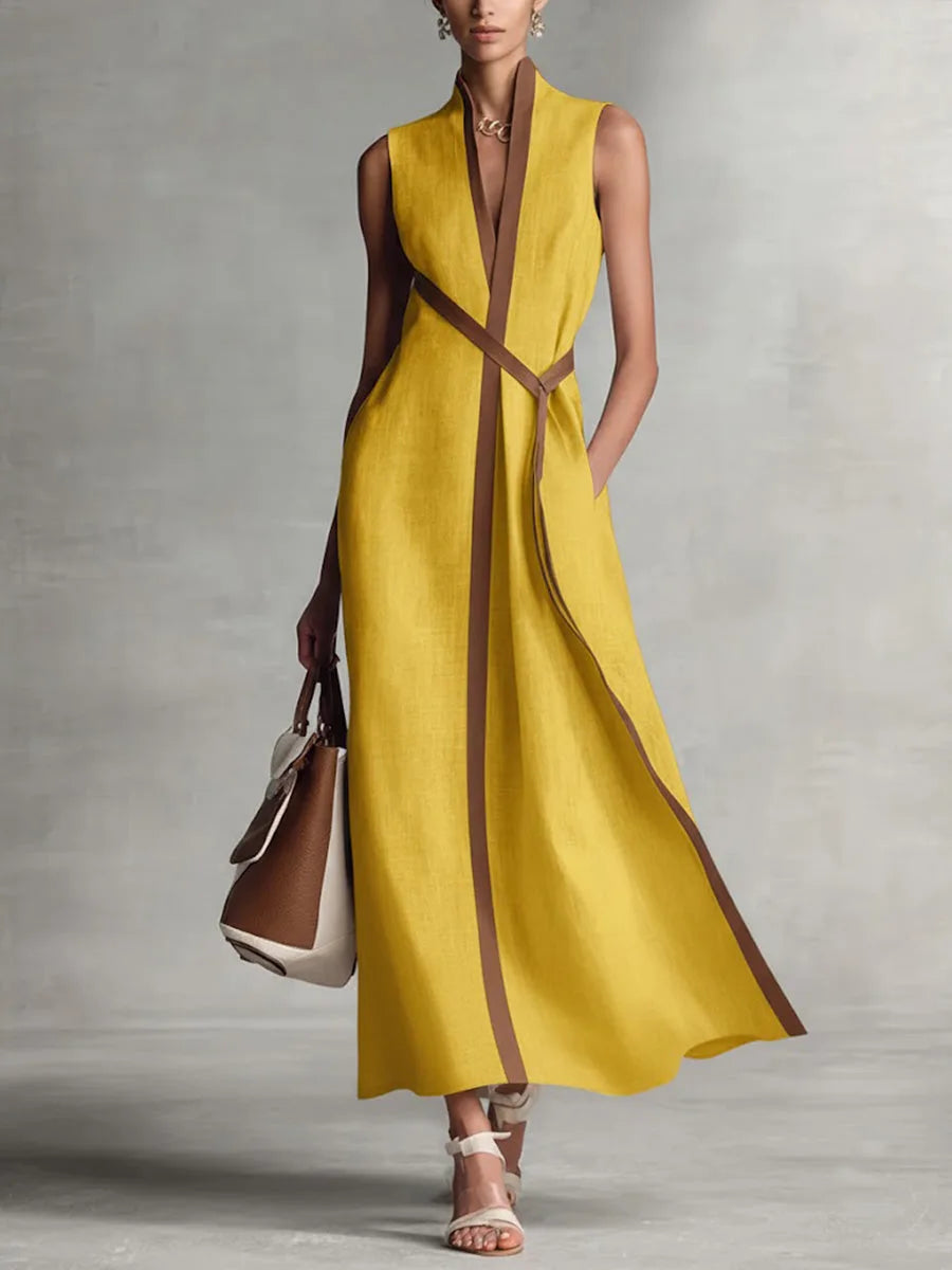 Mustard yellow sleeveless maxi dress with tan piping detail and self-tie waist, worn with nude sandals