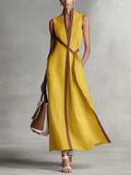 Mustard yellow sleeveless maxi dress with tan piping detail and self-tie waist, worn with nude sandals