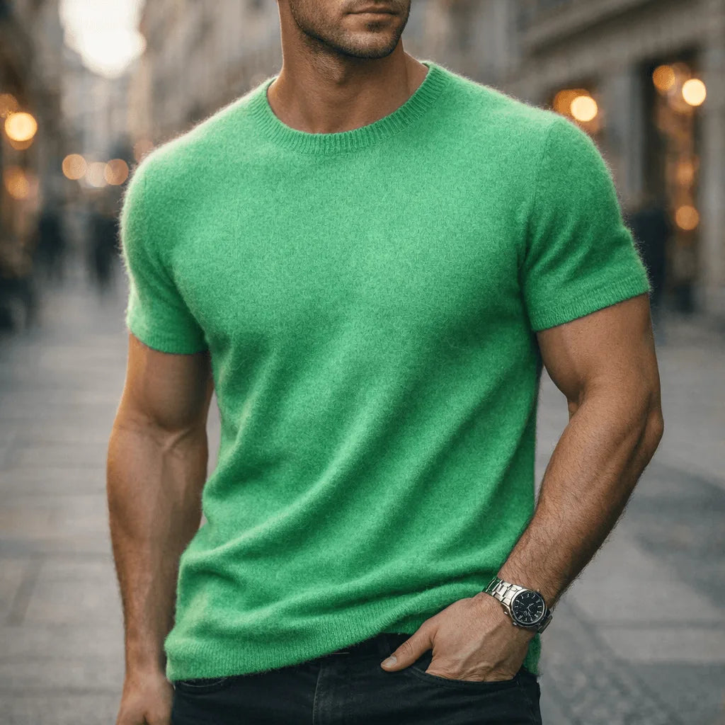 Man wearing a green short-sleeve knit tee with a ribbed crew neckline, styled with dark denim on a city street