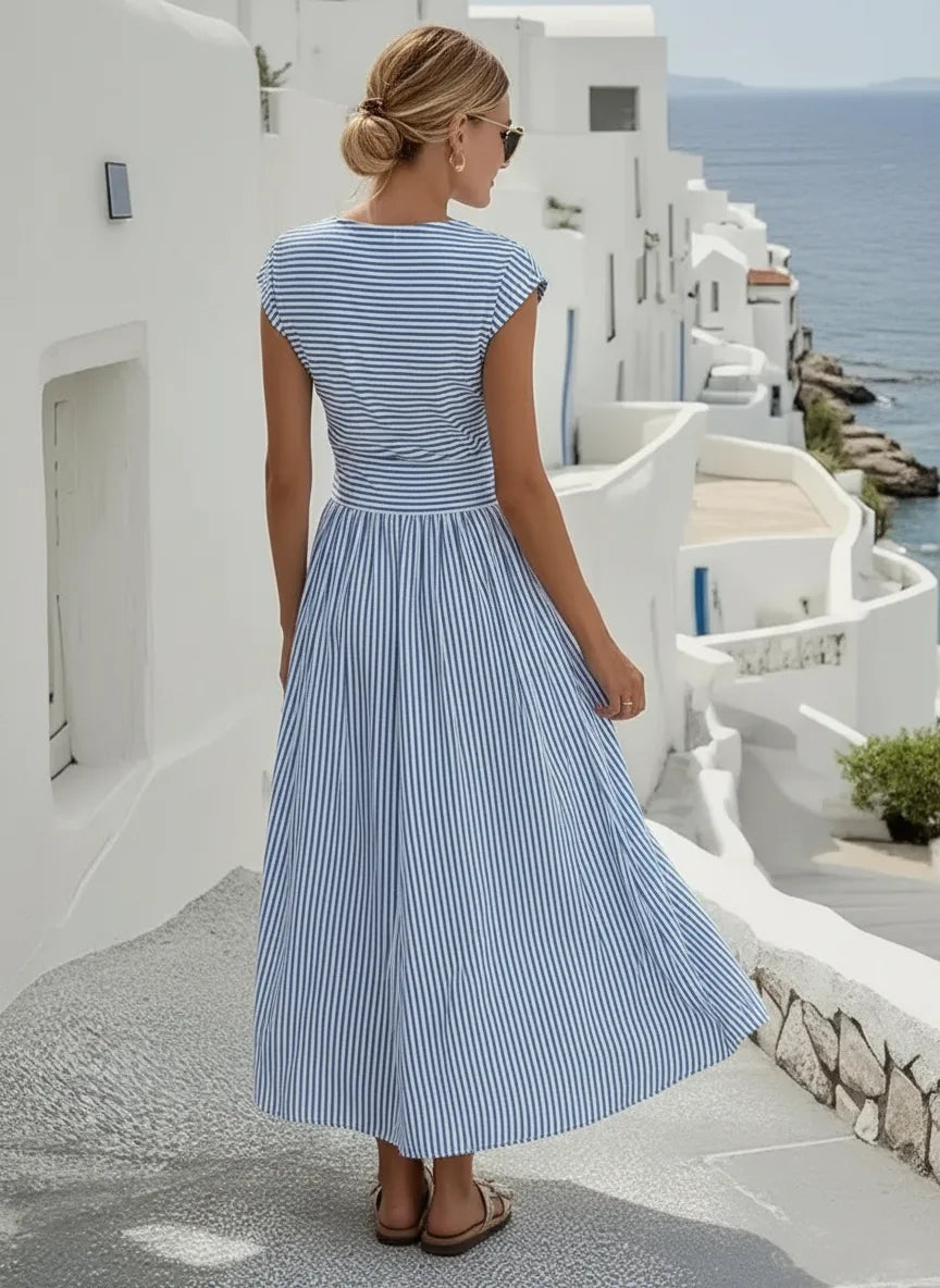 Back view of the striped maxi dress highlighting the flowing skirt and relaxed cap sleeve silhouette by the sea.
