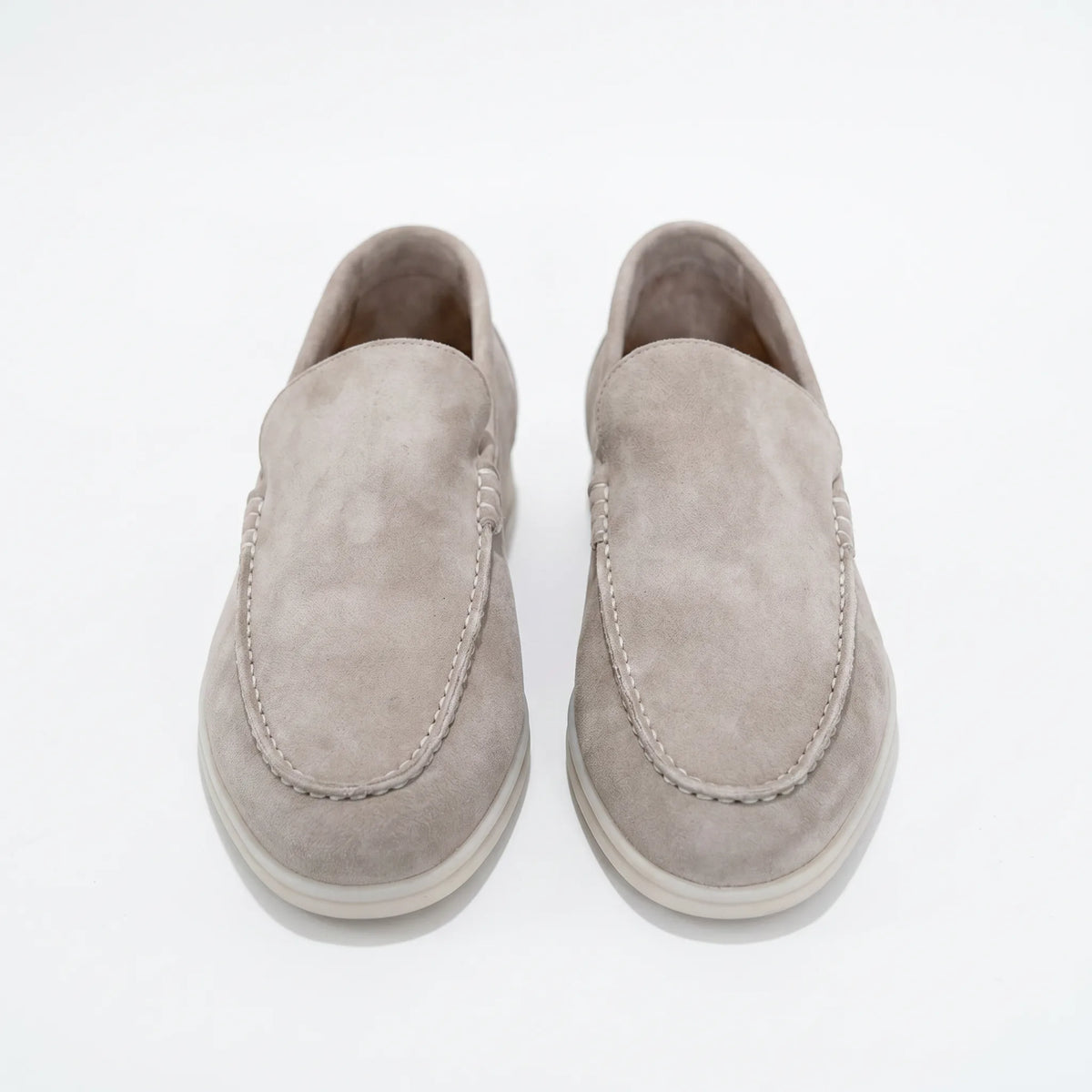 Top-down view of a pair of light grey suede loafers with visible knotted vamp stitch