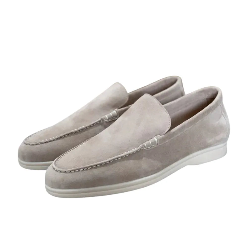 Angled view of grey suede loafers in a pair, showing white outsole and rounded toe