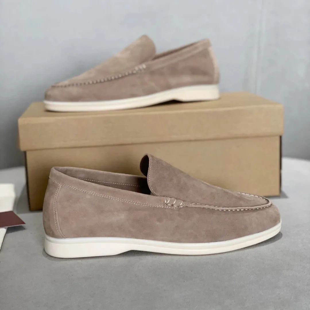 Front angle of grey suede loafers resting against a plain backdrop, white sole visible
