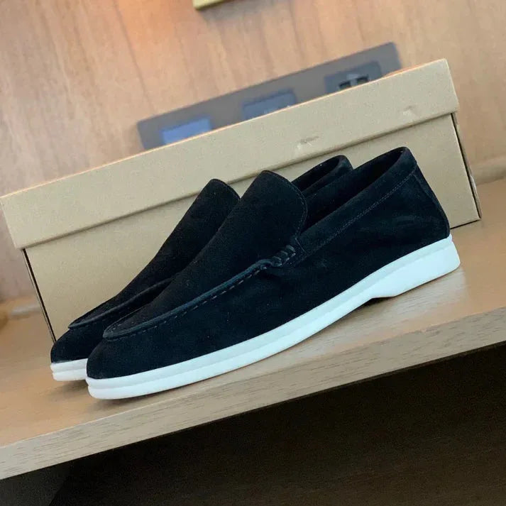 Side view of a pair of taupe suede loafers styled beside the original shoe box